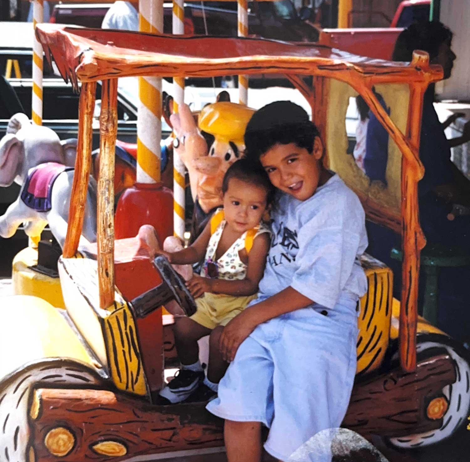 Photo of Crist Morillon and her older brother in a Flintstones car.