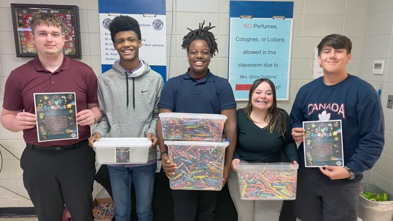 Photo of 5 students posing with boxes of crayons.