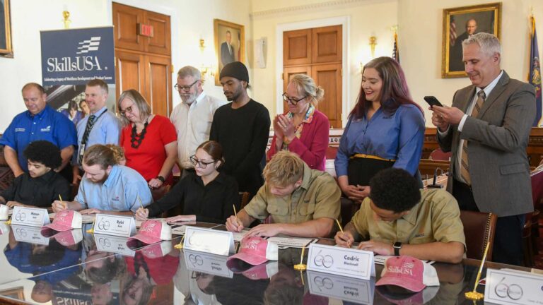 Several students signing on to a skilled trade career. Their advisors and parents look on.